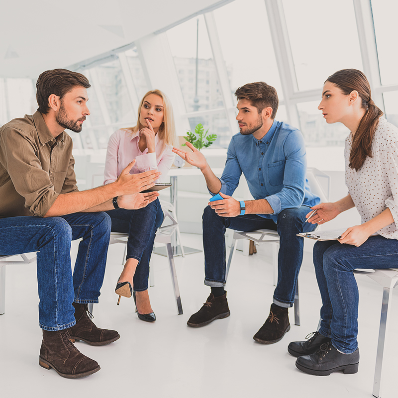 Four adults sitting in a circle engaged in thoughtful discussion